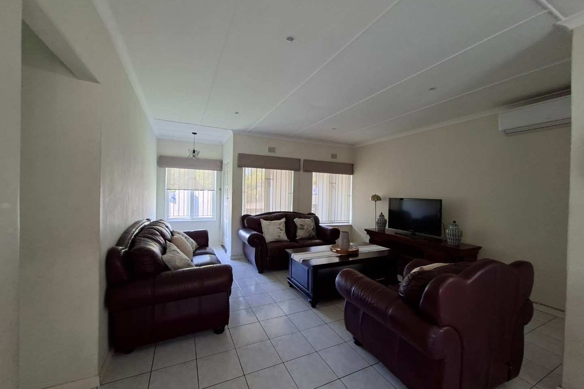 A spacious living room featuring neutral tiled flooring, recessed lighting, and a wall-mounted air conditioning unit, offering a functional and comfortable living space.