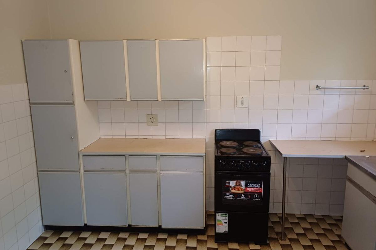 A functional kitchen space featuring built-in cabinetry, a tiled backsplash, and a freestanding stove, offering a blank canvas for potential modern updates.