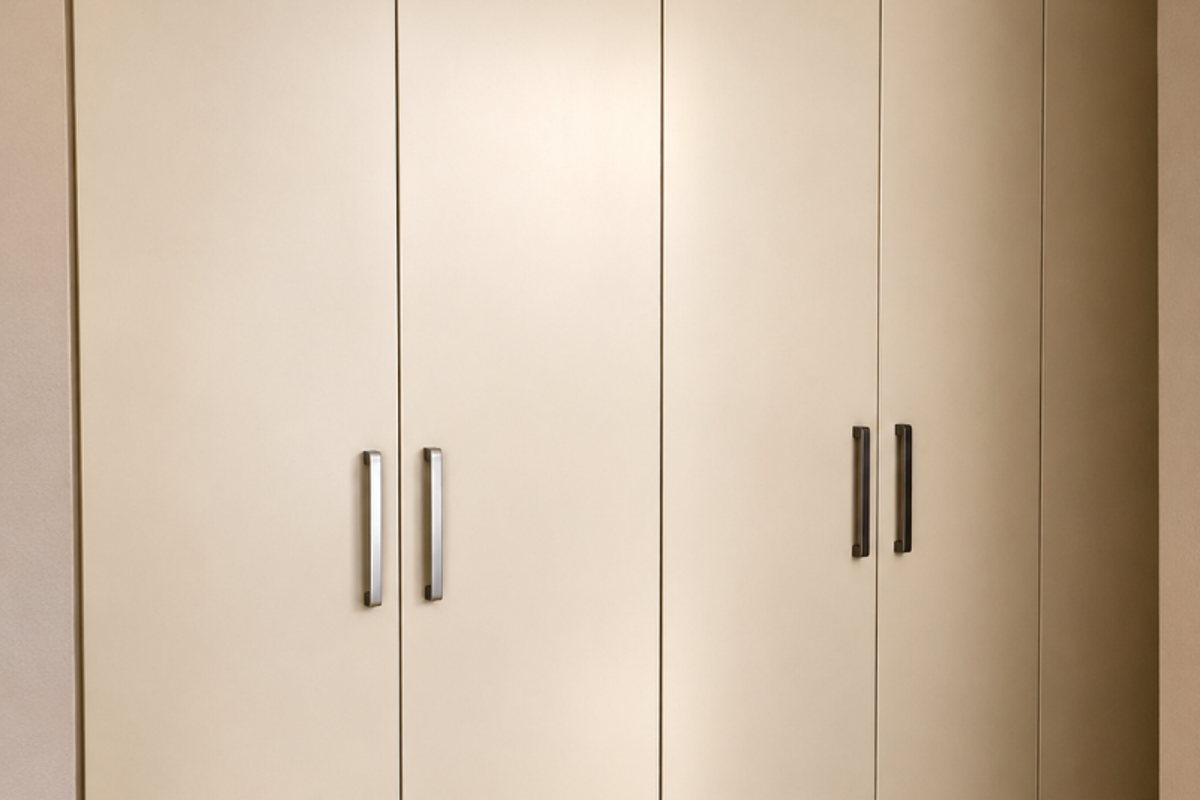 A clean, modern bedroom featuring floor-to-ceiling built-in cupboards with neutral finishes and tiled flooring.