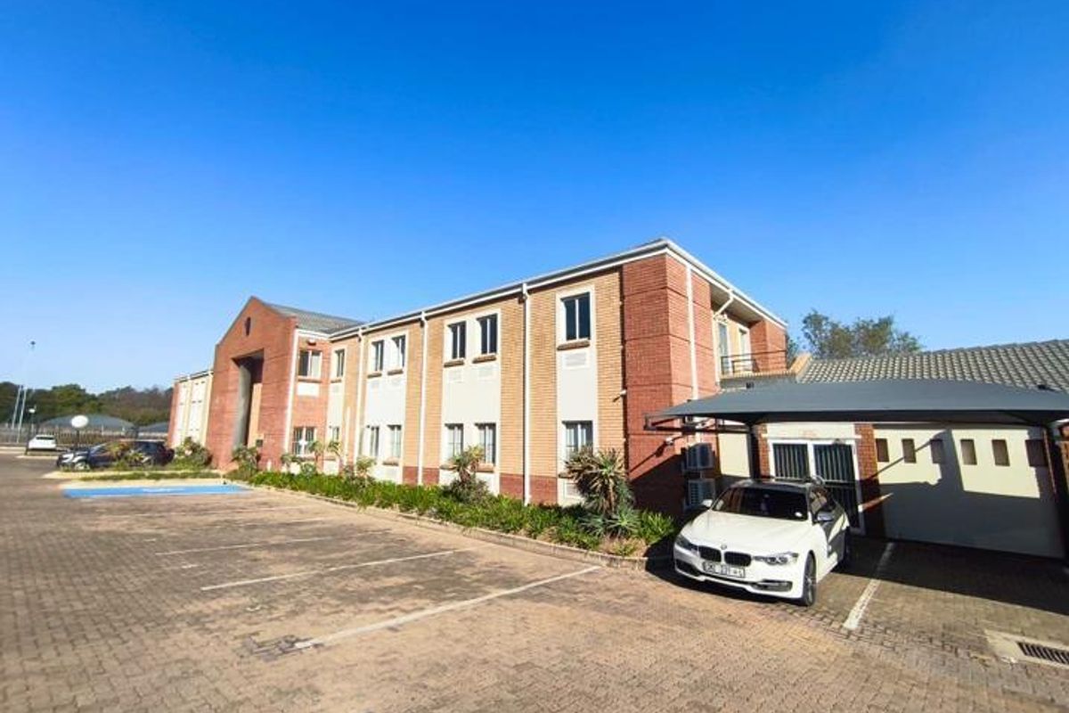 A well-maintained multi-story office building featuring a brick facade, tiled roof, and dedicated paved parking area with a covered carport.