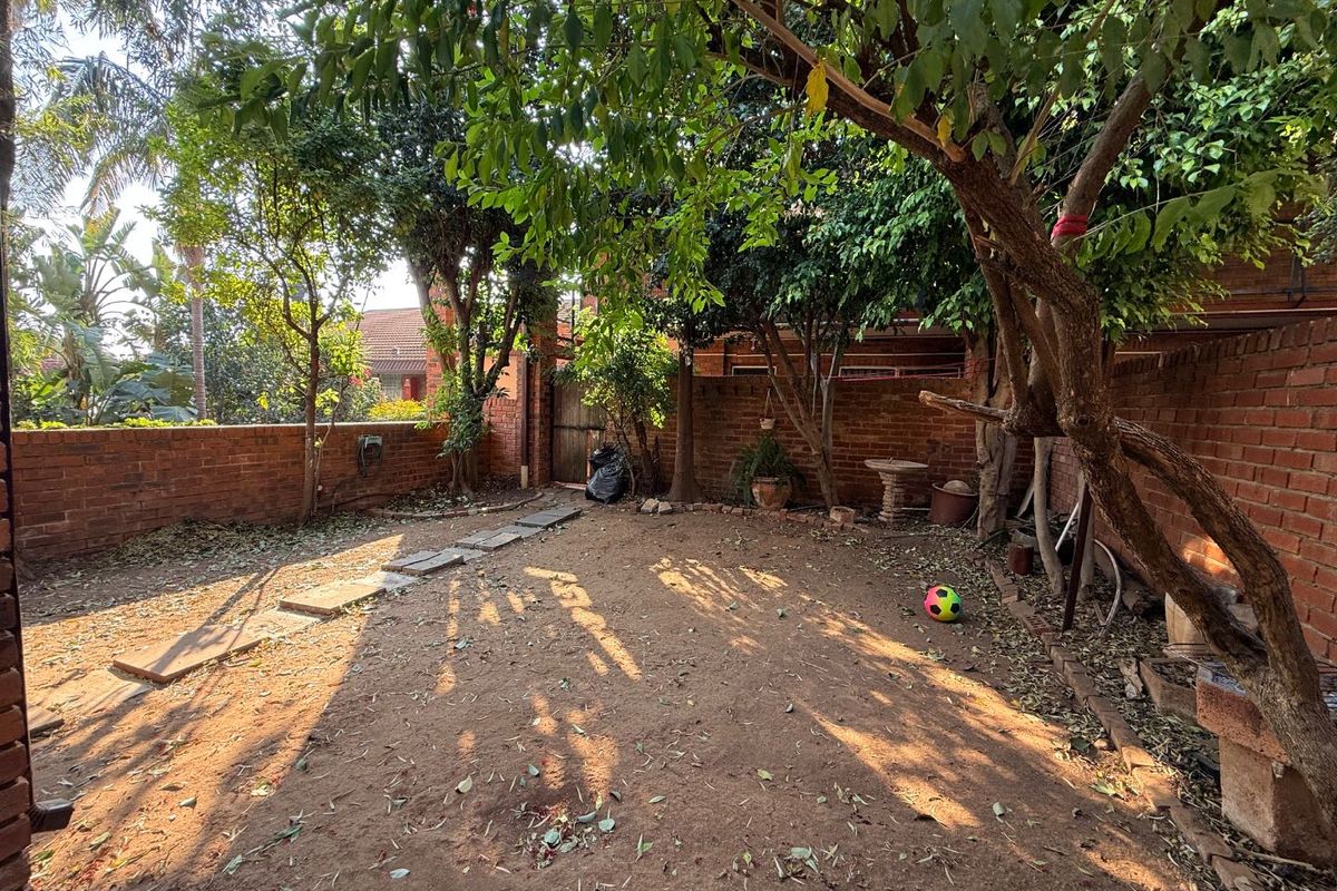 A private rear garden area featuring brick boundary walls, mature trees, and a natural earth ground surface with stone pathway accents.