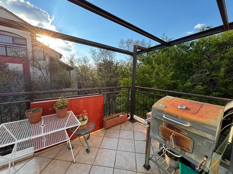 An outdoor balcony featuring a metal pergola frame, tiled flooring, and a metal balustrade, offering an open-air space with views of surrounding greenery.