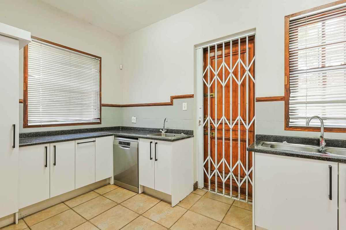 A functional kitchen featuring granite countertops, white cabinetry, double sink, and a secure exterior door with a metal security gate.