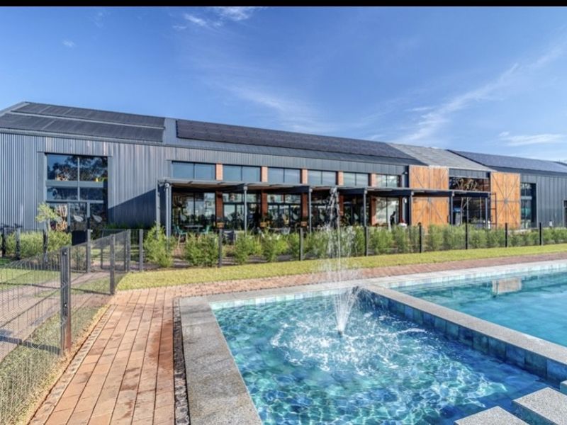 A well-maintained outdoor pool area featuring a water fountain, paved walkways, and modern architectural building with solar panels and covered patio space.