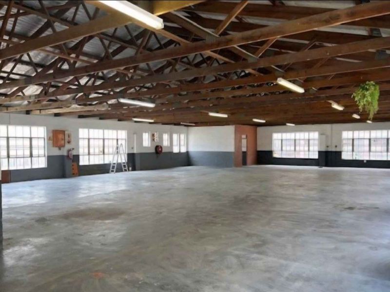 Spacious industrial utility area featuring exposed timber roof trusses, large steel-framed windows, and durable concrete flooring, suitable for various commercial or storage applications.