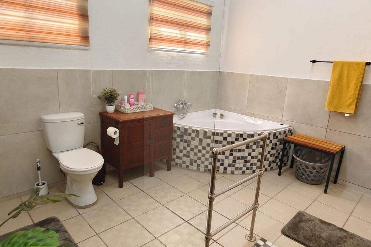 A functional bathroom featuring a corner bathtub with mosaic tiling, a pedestal basin, and neutral wall tiles.