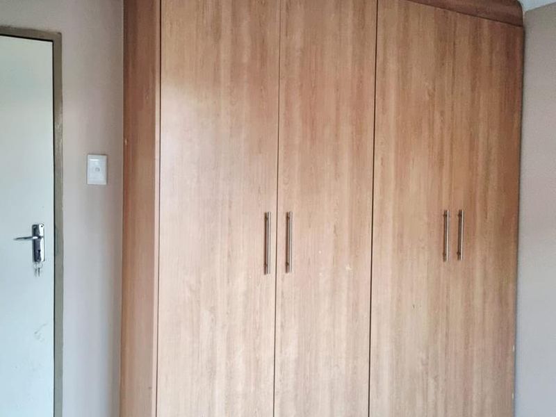 A bedroom featuring a large, wood-finish built-in wardrobe, tiled flooring, and a standard internal door.