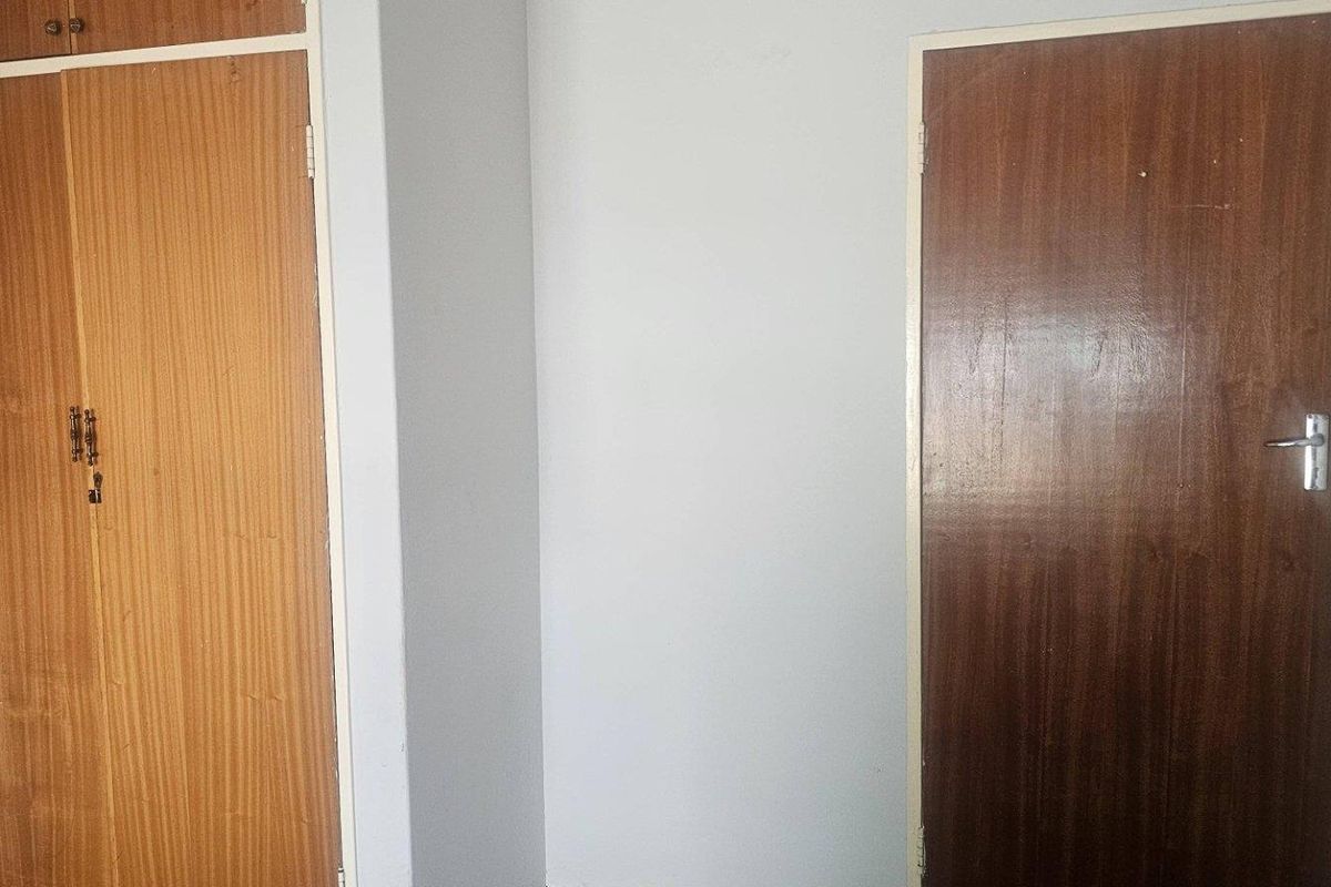 A bedroom interior featuring built-in wooden cupboards and a standard wooden door, showing signs of age and wear.