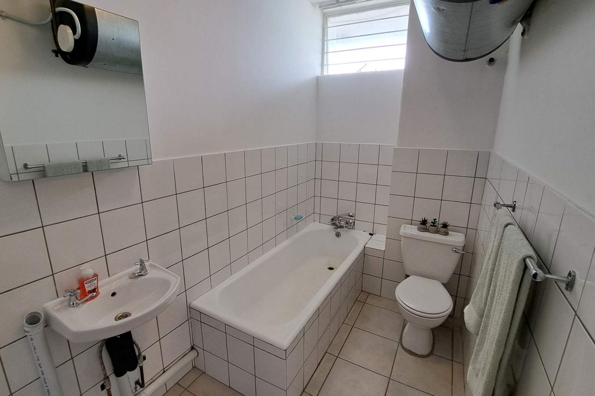 A functional bathroom featuring a standard bathtub, pedestal sink, and toilet with white wall tiling and a high-level window for natural light.