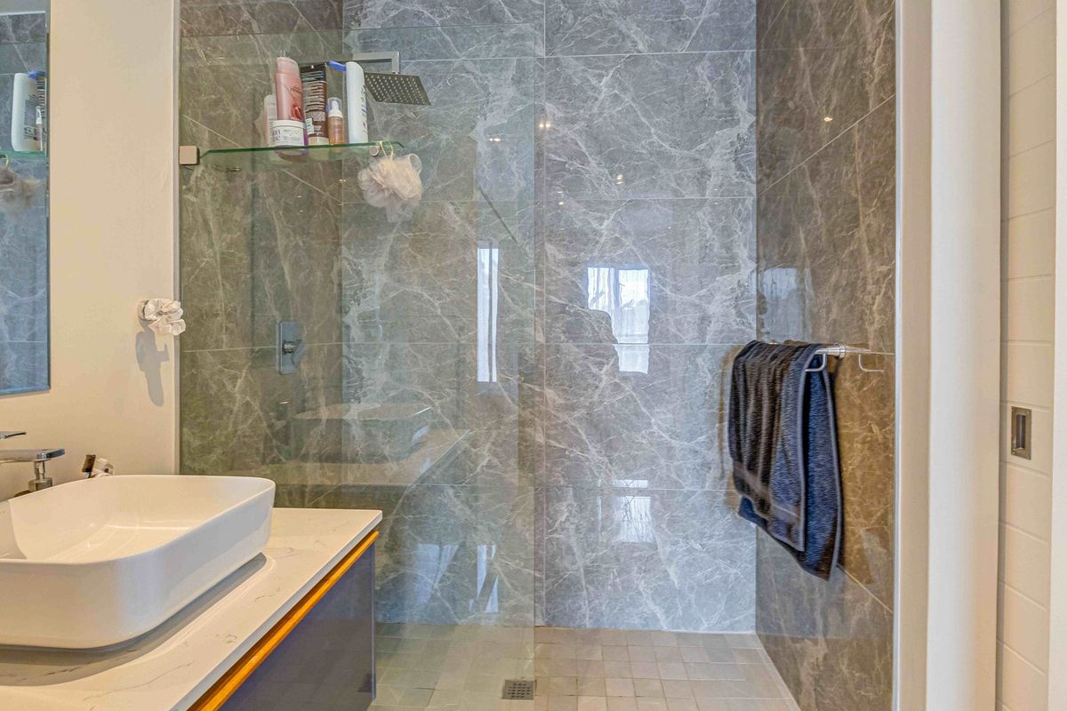Modern bathroom featuring a walk-in shower with grey marble-effect wall tiles, a rain shower head, and a contemporary vessel sink on a vanity unit.