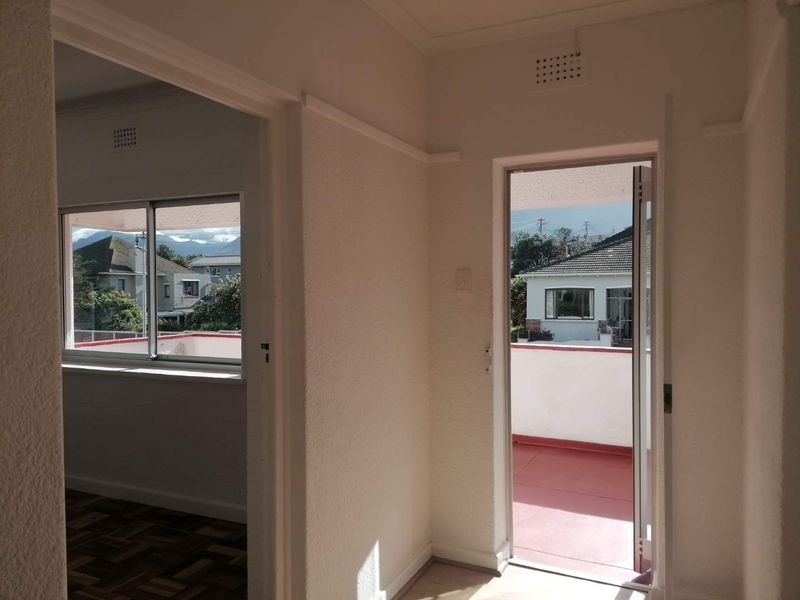 A bright, empty hallway featuring parquet flooring and direct access to an outdoor balcony area with neighborhood views.