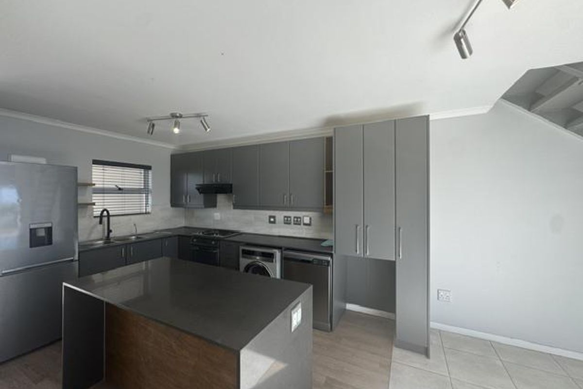 Modern kitchen featuring grey cabinetry, stone countertops, a central island, and integrated appliances, offering a clean and functional workspace.