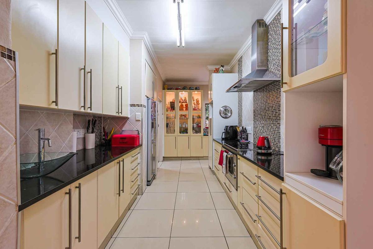 A galley-style kitchen featuring cream cabinetry, dark granite countertops, a stainless steel extractor fan, and tiled flooring.