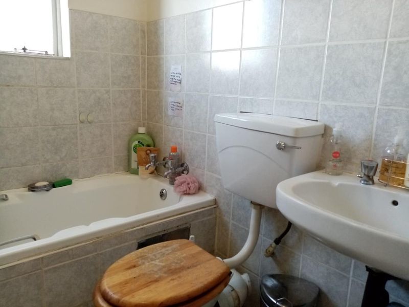 A functional bathroom featuring a standard bathtub, pedestal basin, and toilet with dated ceramic wall tiling.