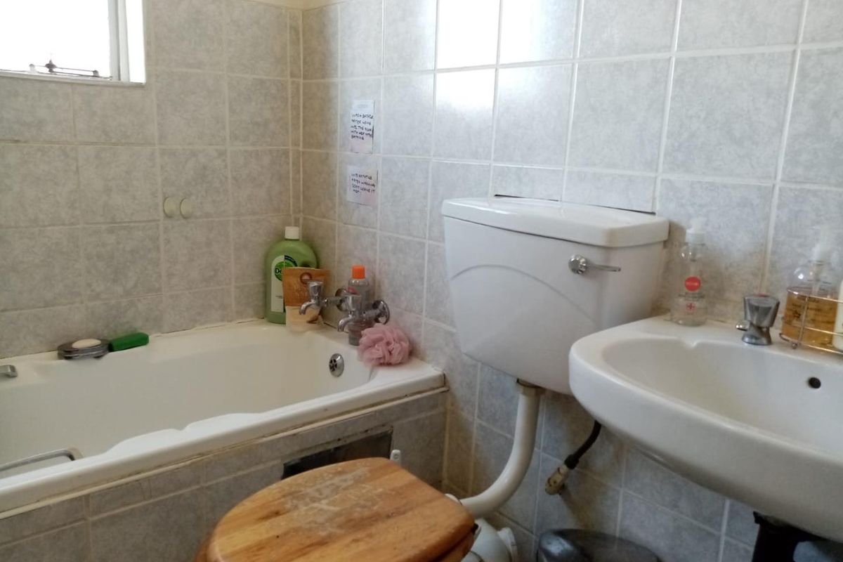 A functional bathroom featuring a standard bathtub, pedestal basin, and toilet with dated ceramic wall tiling.