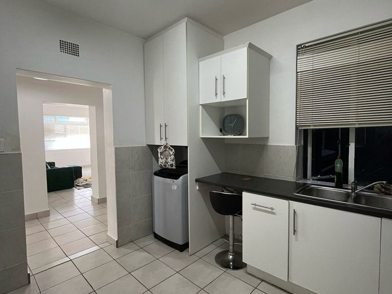 A functional scullery area featuring built-in white cabinetry, a stainless steel sink, tiled flooring, and a tiled splashback, providing practical utility space.