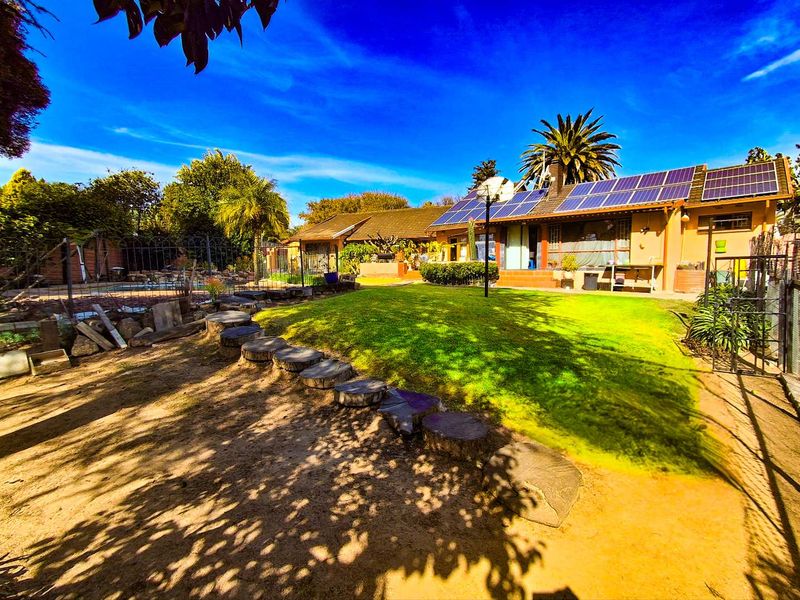 Rear view of the house featuring a large lawn, solar panel installation on the roof, and a fenced garden area.
