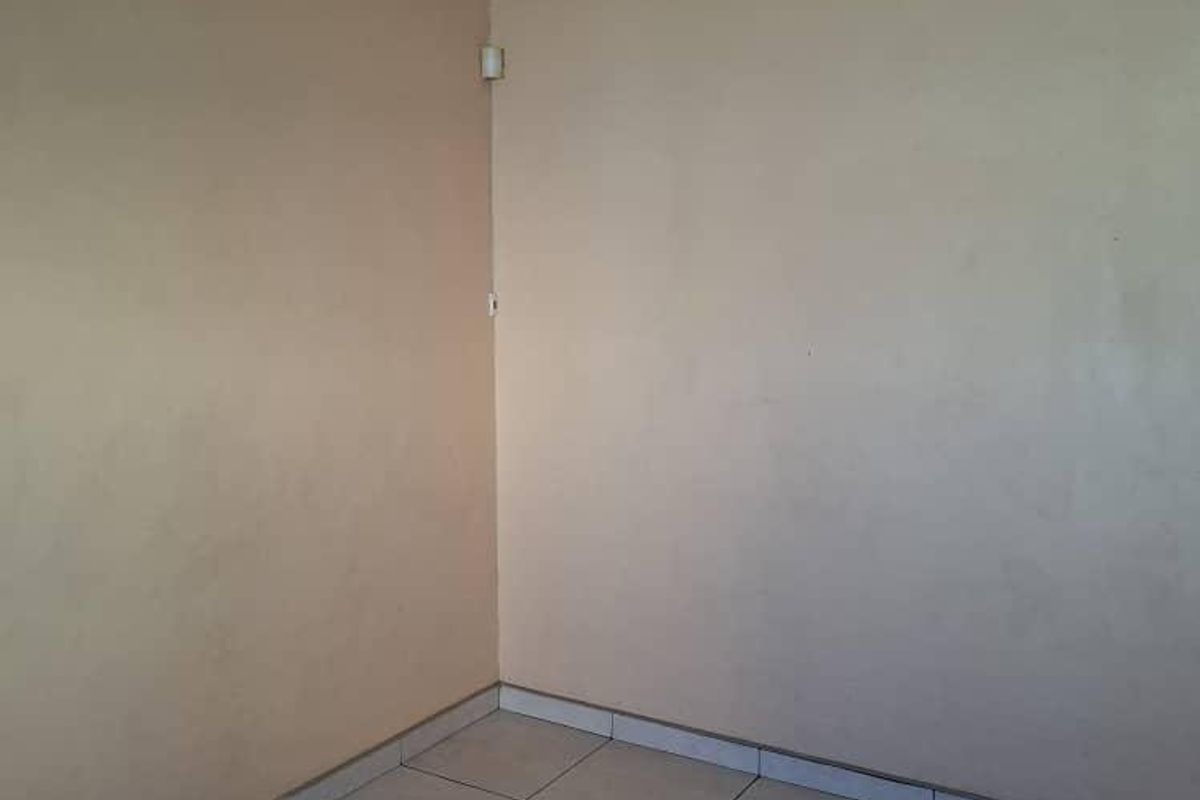 An empty corner of a room featuring neutral tiled flooring and plain painted walls with simple ceiling cornicing.