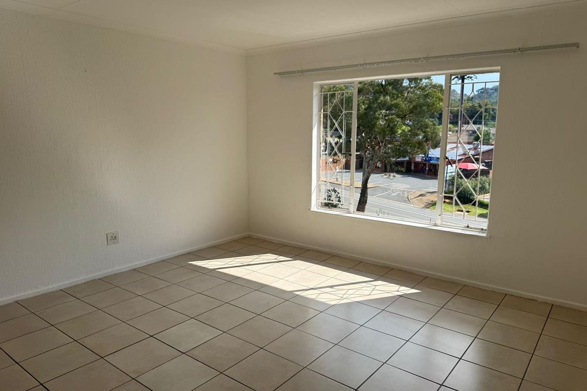 A bright, empty bedroom featuring tiled flooring, a large window with security bars, and a curtain rail, offering a view of the street.