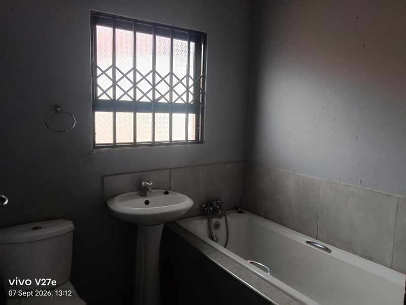 A functional bathroom featuring a pedestal basin, bathtub, and toilet, with security bars on the window and tiled splashback areas.