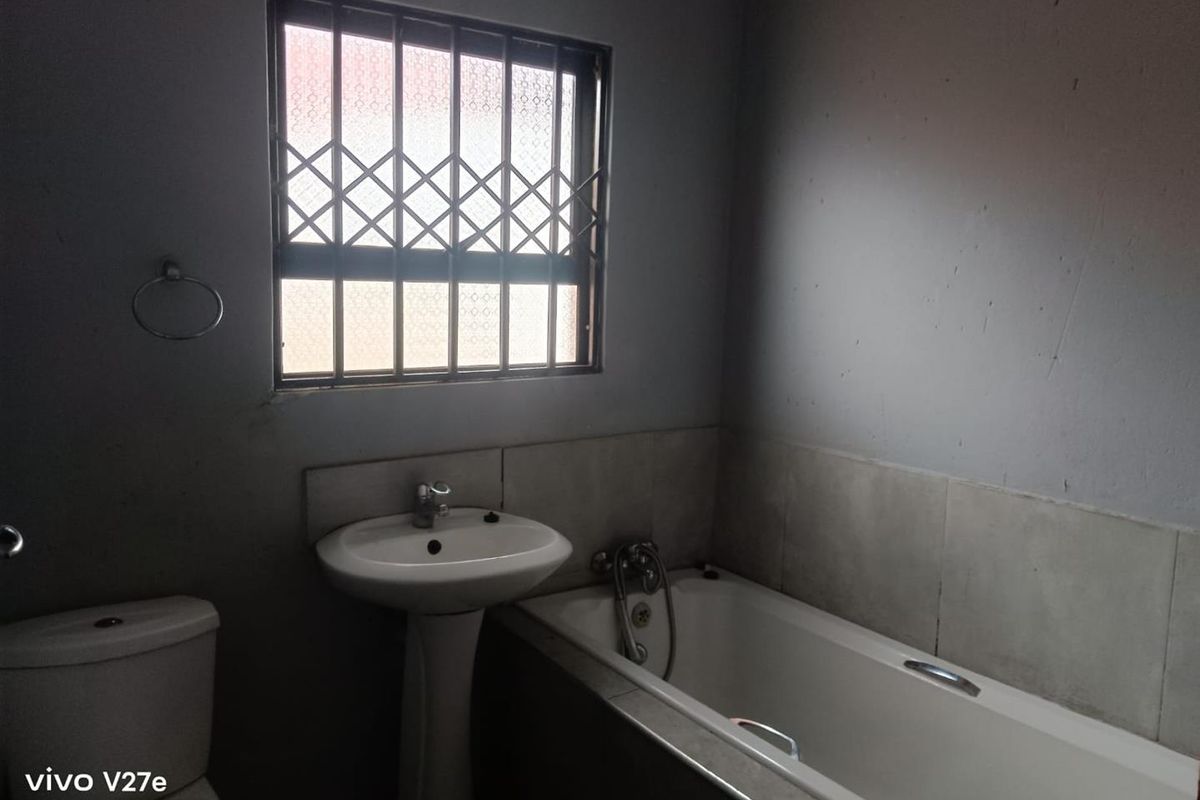 A functional bathroom featuring a pedestal basin, bathtub, and toilet, with security bars on the window and tiled splashback areas.