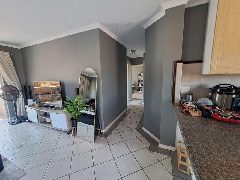 Open plan living area featuring tiled floors, grey walls, and a functional kitchen with granite countertops, leading into a hallway.