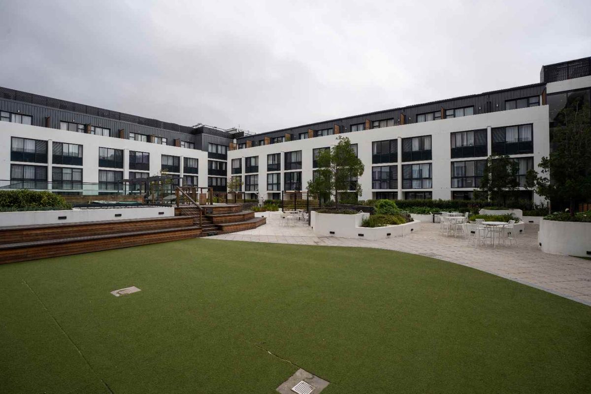 A well-maintained communal courtyard featuring artificial turf, raised timber decking, paved areas, and built-in planters, surrounded by the apartment building facade.