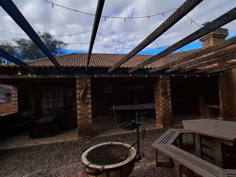 Covered outdoor patio area featuring brick pillars, a timber pergola, and a built-in braai, perfect for outdoor entertaining.