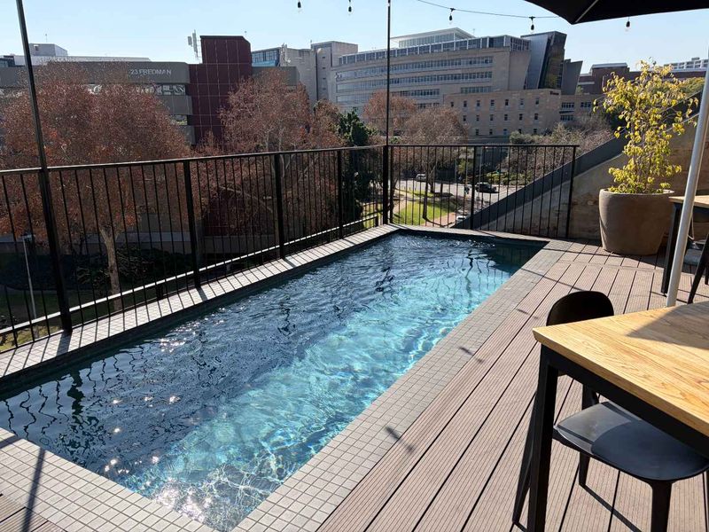 A modern rooftop plunge pool area featuring timber decking, a sleek metal balustrade, and urban city views.