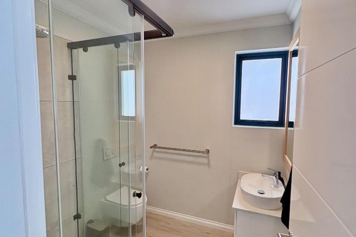 Modern bathroom featuring a glass shower enclosure, wall-hung toilet, and a sleek vanity with a vessel sink, finished with light wood-look flooring.