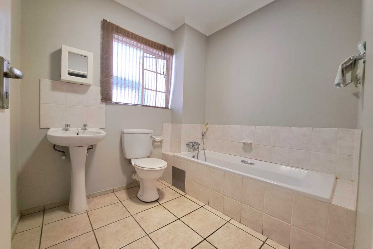 A functional bathroom featuring a pedestal basin, toilet, and a built-in bathtub with tiled splashbacks and flooring.