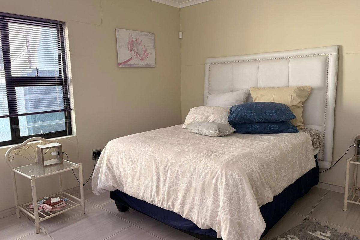 A functional bedroom featuring tiled flooring, neutral wall tones, and an aluminium-framed window with venetian blinds.
