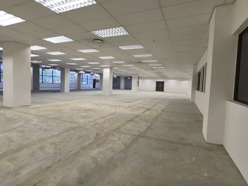 Expansive open-plan retail or office space featuring a suspended ceiling, recessed lighting, structural columns, and large windows, currently in a shell condition.