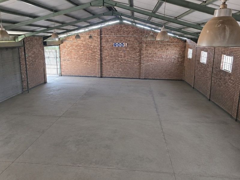 Spacious industrial utility space featuring exposed brick walls, concrete flooring, and high steel truss ceilings with industrial pendant lighting.