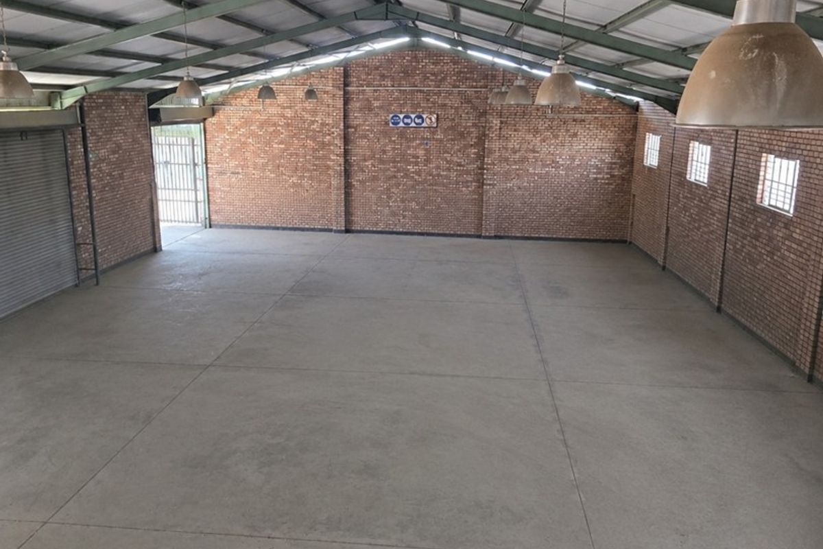 Spacious industrial utility space featuring exposed brick walls, concrete flooring, and high steel truss ceilings with industrial pendant lighting.