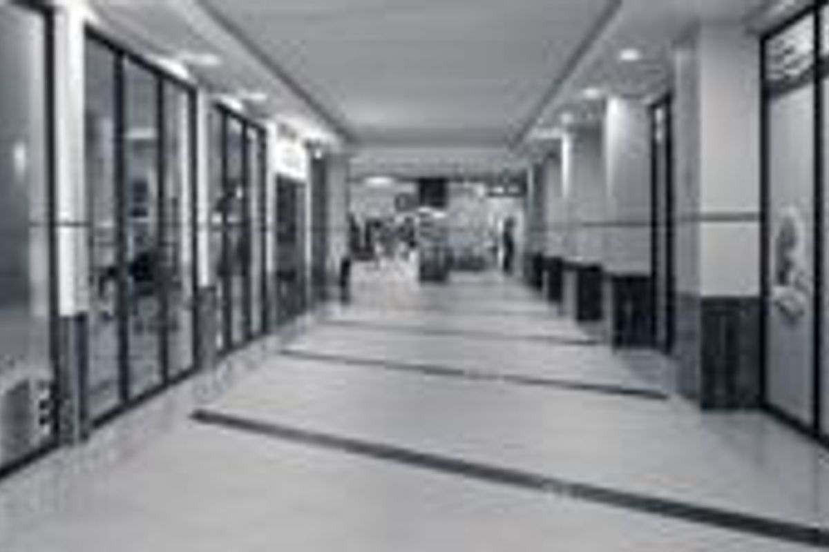 A well-maintained retail corridor featuring glass storefronts, tiled flooring, and recessed lighting within a commercial shopping center.