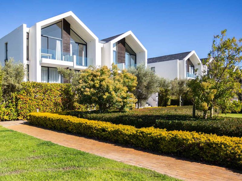 Modern apartment complex featuring striking pitched roof architecture, glass balconies, and well-maintained landscaped gardens with a paved walkway.
