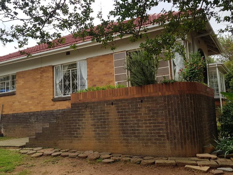 Rear view of a brick cottage featuring a tiled roof, security window grilles, and a raised brick retaining wall with concrete steps.