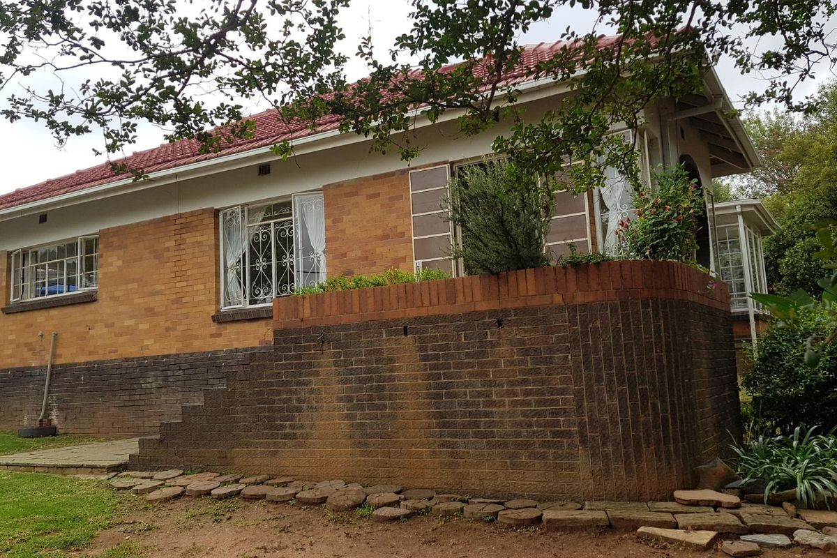 Rear view of a brick cottage featuring a tiled roof, security window grilles, and a raised brick retaining wall with concrete steps.