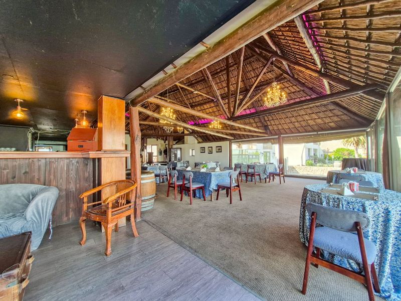 Spacious open-plan entertainment area featuring a traditional thatched roof, exposed timber beams, and a built-in bar, with large glass doors opening to the exterior.