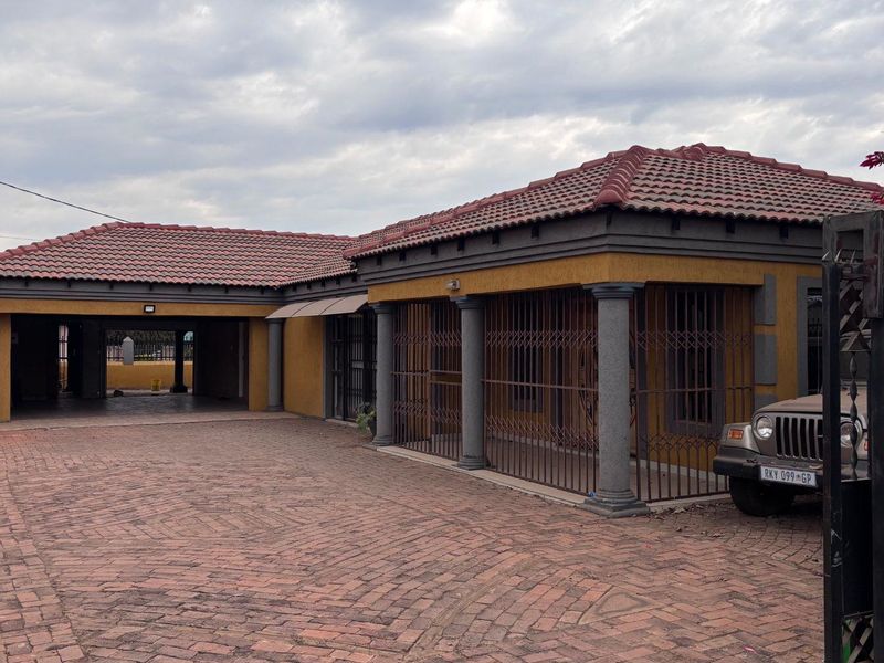 Front view of a residential property featuring a paved driveway, covered carport, and secure gated entrance with a tiled roof finish.