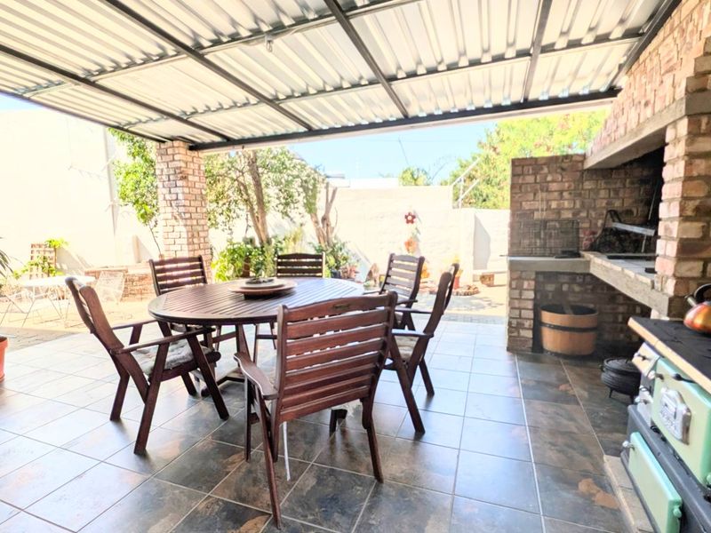 Covered outdoor patio featuring a built-in brick braai, tiled flooring, and a corrugated metal roof, ideal for alfresco dining and entertaining.