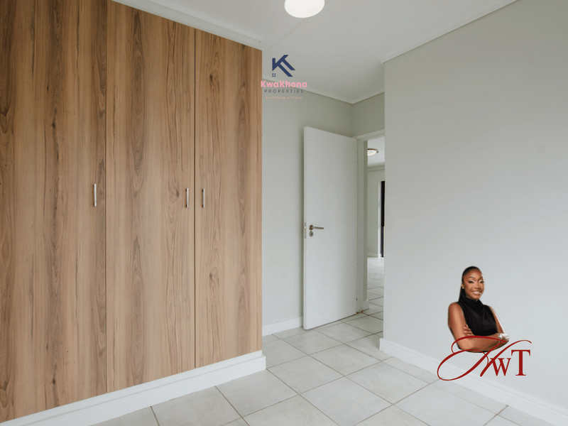 A clean, empty bedroom featuring modern wood-finish built-in cupboards, neutral wall paint, and light-colored floor tiles.