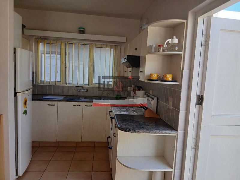 A compact kitchen featuring laminate countertops, a double basin sink, built-in cabinetry, and tiled flooring, offering a functional layout with potential for modernization.