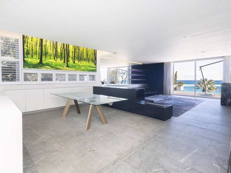 Spacious open-plan living area featuring modern stone tile flooring, built-in cabinetry, and expansive sliding glass doors offering panoramic ocean views.