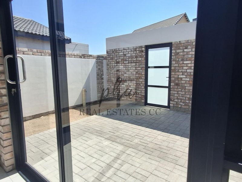 A private, paved outdoor patio area enclosed by brick boundary walls, featuring a modern glass panel door.