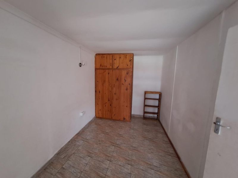 A compact, empty bedroom featuring tiled flooring and a built-in wooden wardrobe, offering a blank canvas for potential updates.