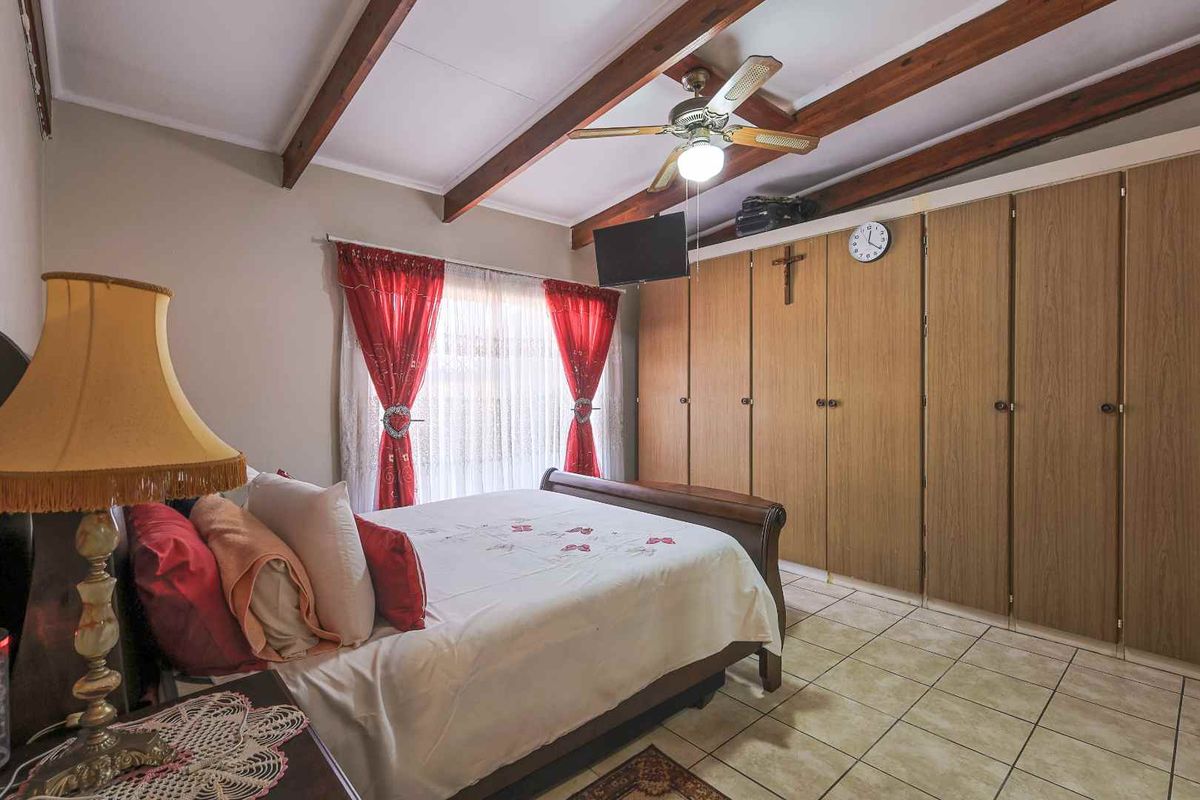 A bedroom featuring built-in wooden cupboards, exposed timber ceiling beams, a ceiling fan, and tiled flooring.