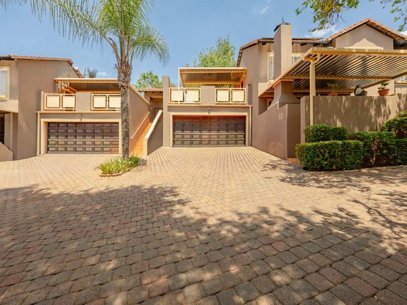 Front elevation of a townhouse featuring a paved driveway, double garage doors, and upper-level balconies with pergola structures.