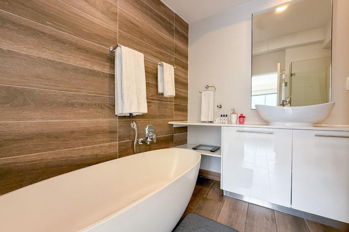 Modern bathroom featuring a freestanding bathtub, wood-look tiled feature wall, white vanity cabinet with vessel sink, and a large wall-mounted mirror.